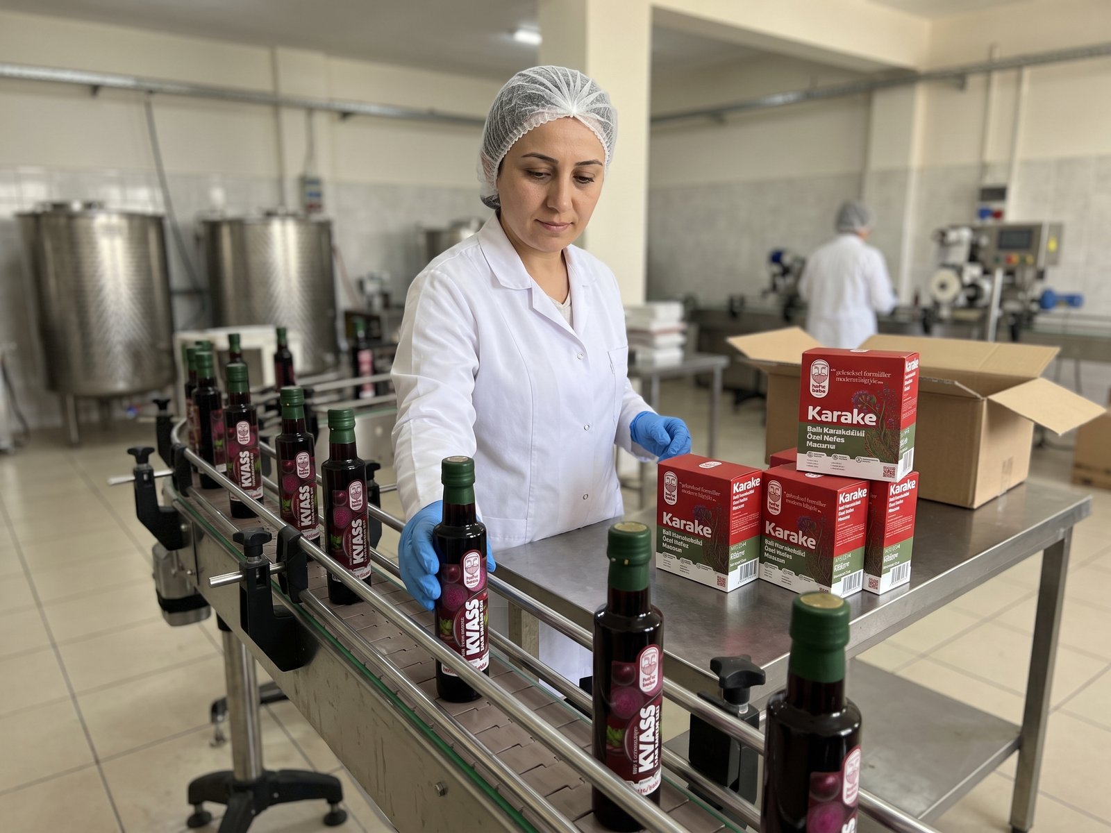 Üretim tesisinde banttan geçen Hafızbaba Kvass şişelerini kontrol eden çalışan ve Karake kutuları.